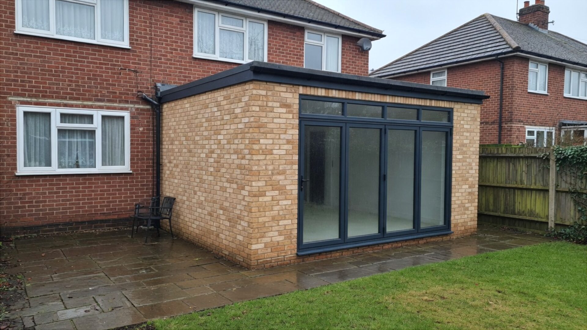 Finished single-storey rear brick extension with anthracite bifold doors on a red-brick house in a British garden